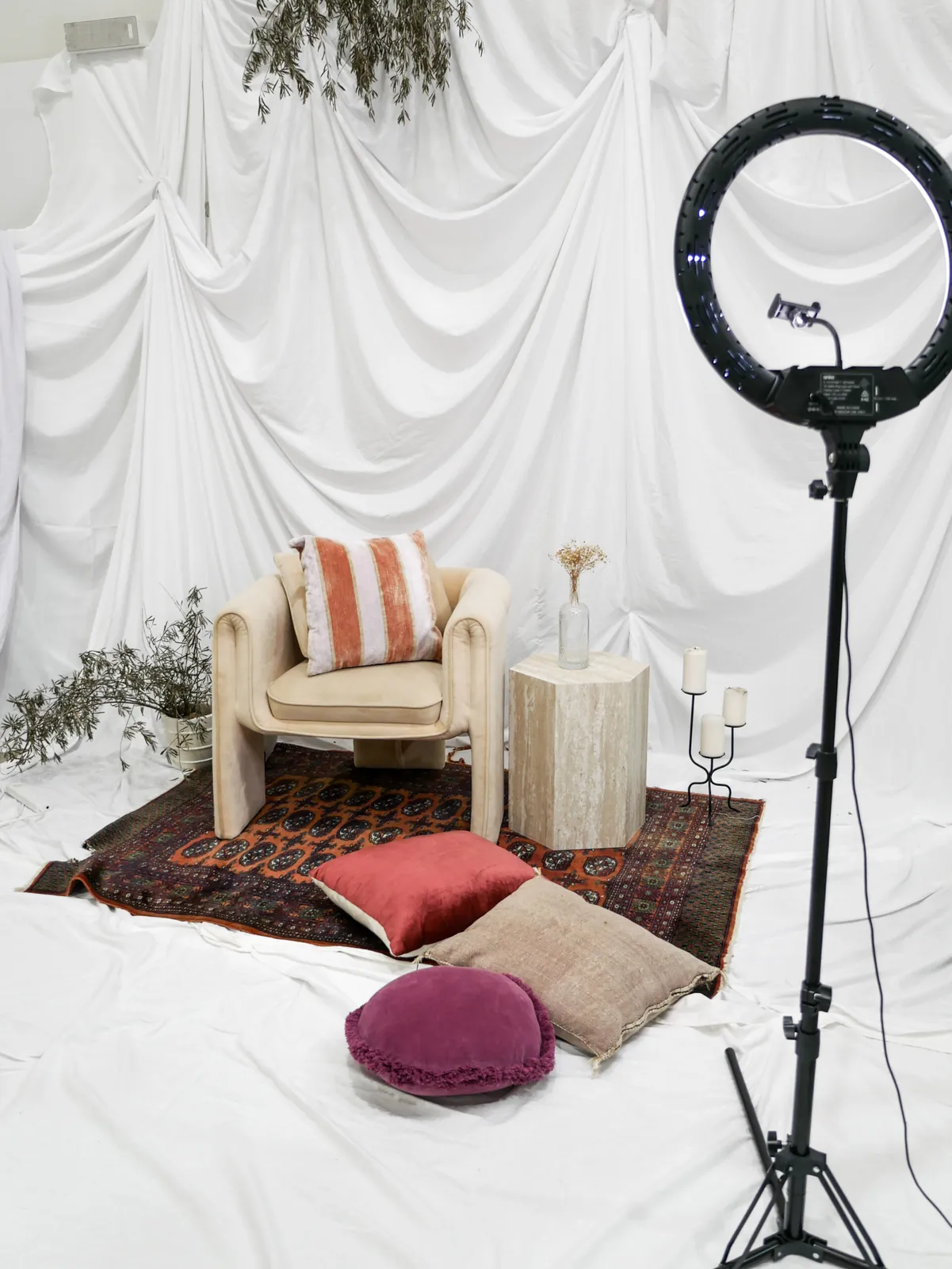 A styled lounge scene on draped white cloth, with a rug, cushions and a ring light, at Birdcage Studios